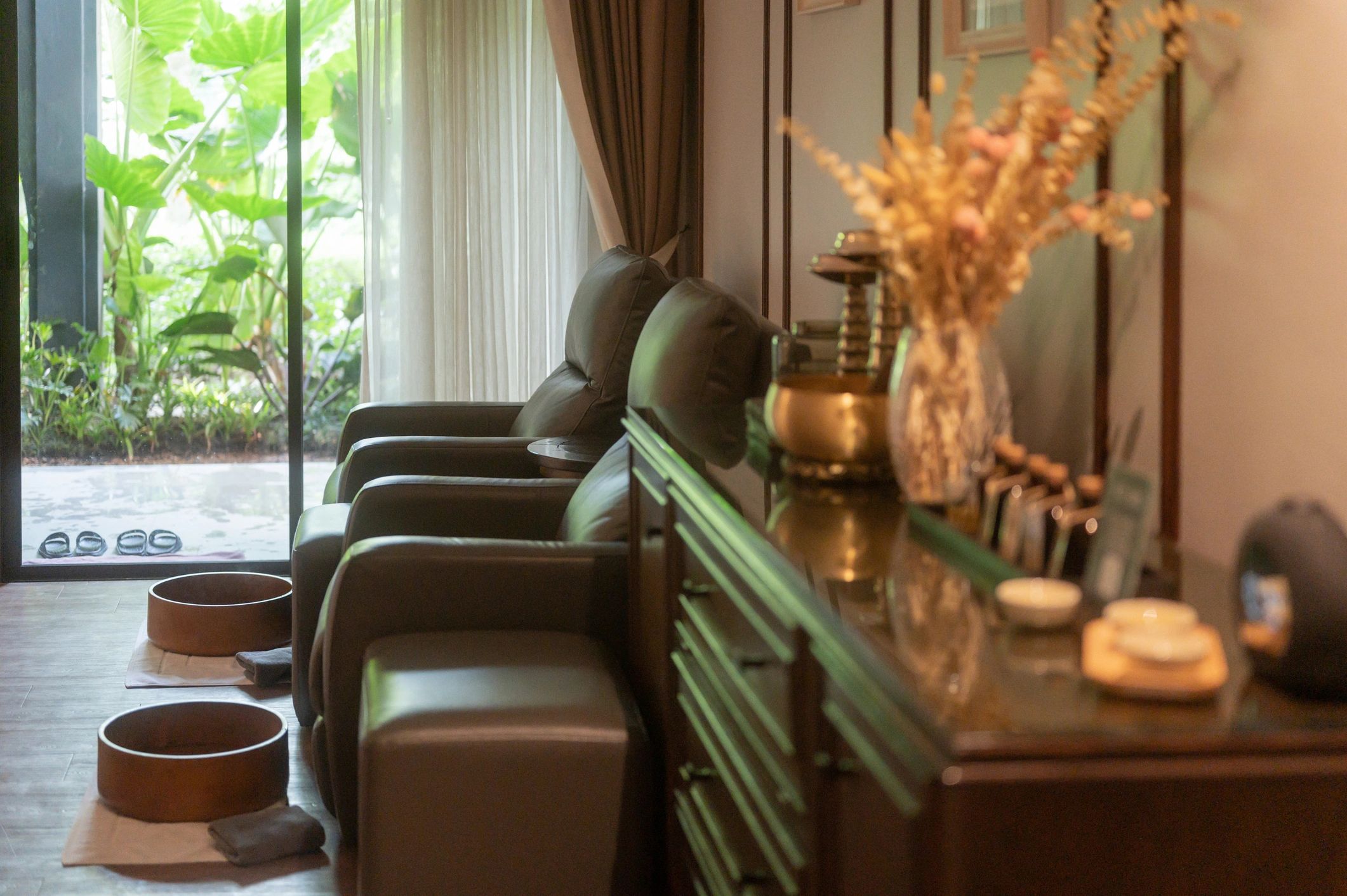 elegant thai spa massage room interior with leather foot massage chairs wooden wash basins and tropical garden background